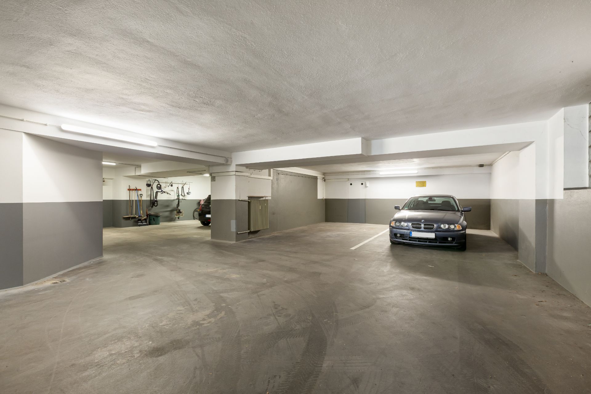 Tiefgarage mit geparktem Auto und Abstellplatz für Fahrräder und Werkzeuge.