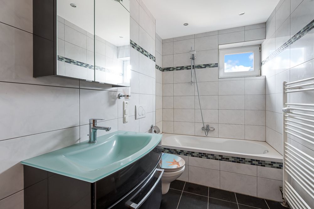 Modernes Badezimmer mit Badewanne, Waschbecken, Spiegel und kleinem Fenster.