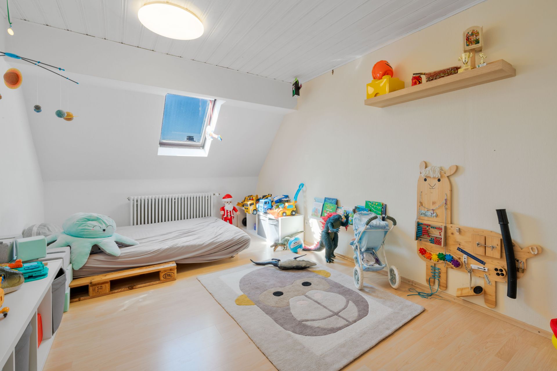 Helles Kinderzimmer mit Spielsachen, einem Bett, Teppich mit Tiermotiv und Dachfenster.