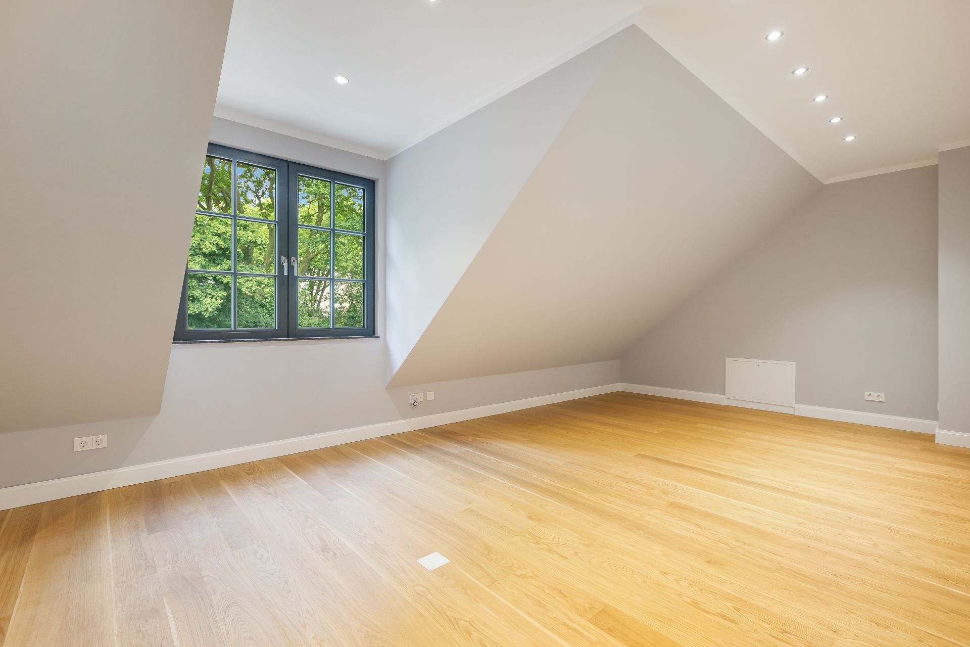 Leeres Zimmer mit Dachschräge, großem Fenster und hellem Holzboden.