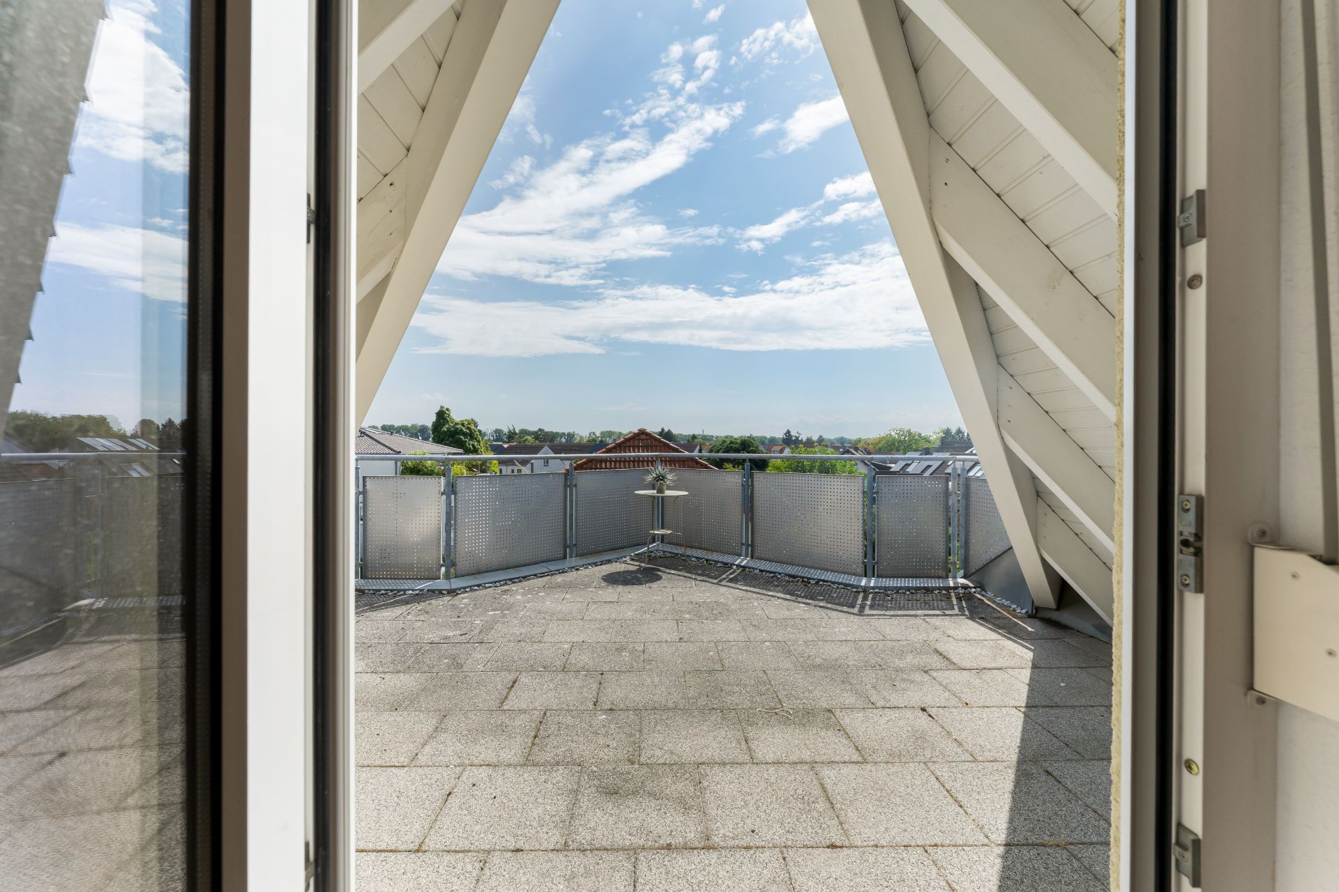 Große Dachterrasse mit grauem Fliesenboden und Blick auf den Himmel und Nachbarhäuser.