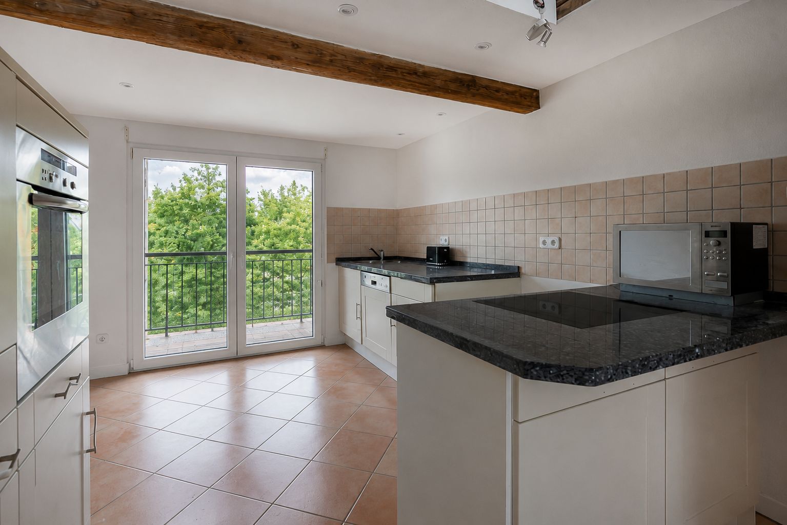 Moderne Küche mit großen Fenstern, weißen Schränken, schwarzen Arbeitsplatten und Geräten.