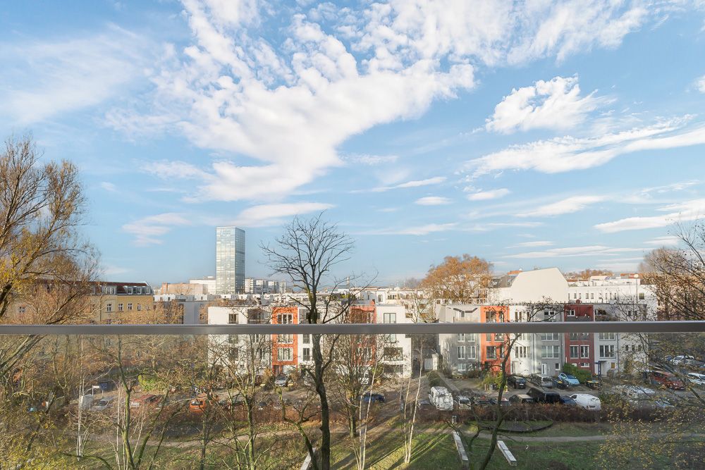 Aussicht vom Balkon auf Wohnhäuser, Bäume und einen Park bei blauem Himmel.
