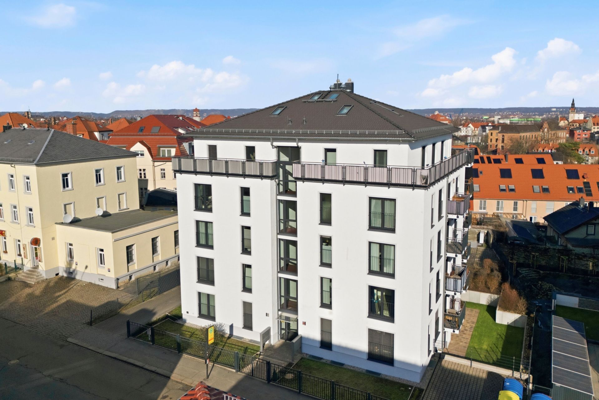 Modernes, weißes Mehrfamilienhaus mit Flachdach und Balkonen, umgeben von weiteren Gebäuden.