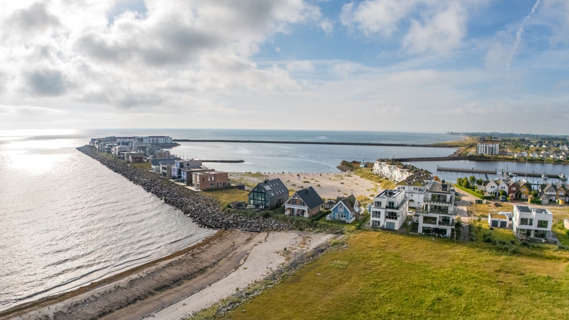 Luftaufnahme von modernen Wohnhäusern an der Küste mit Strand und Meer im Hintergrund.