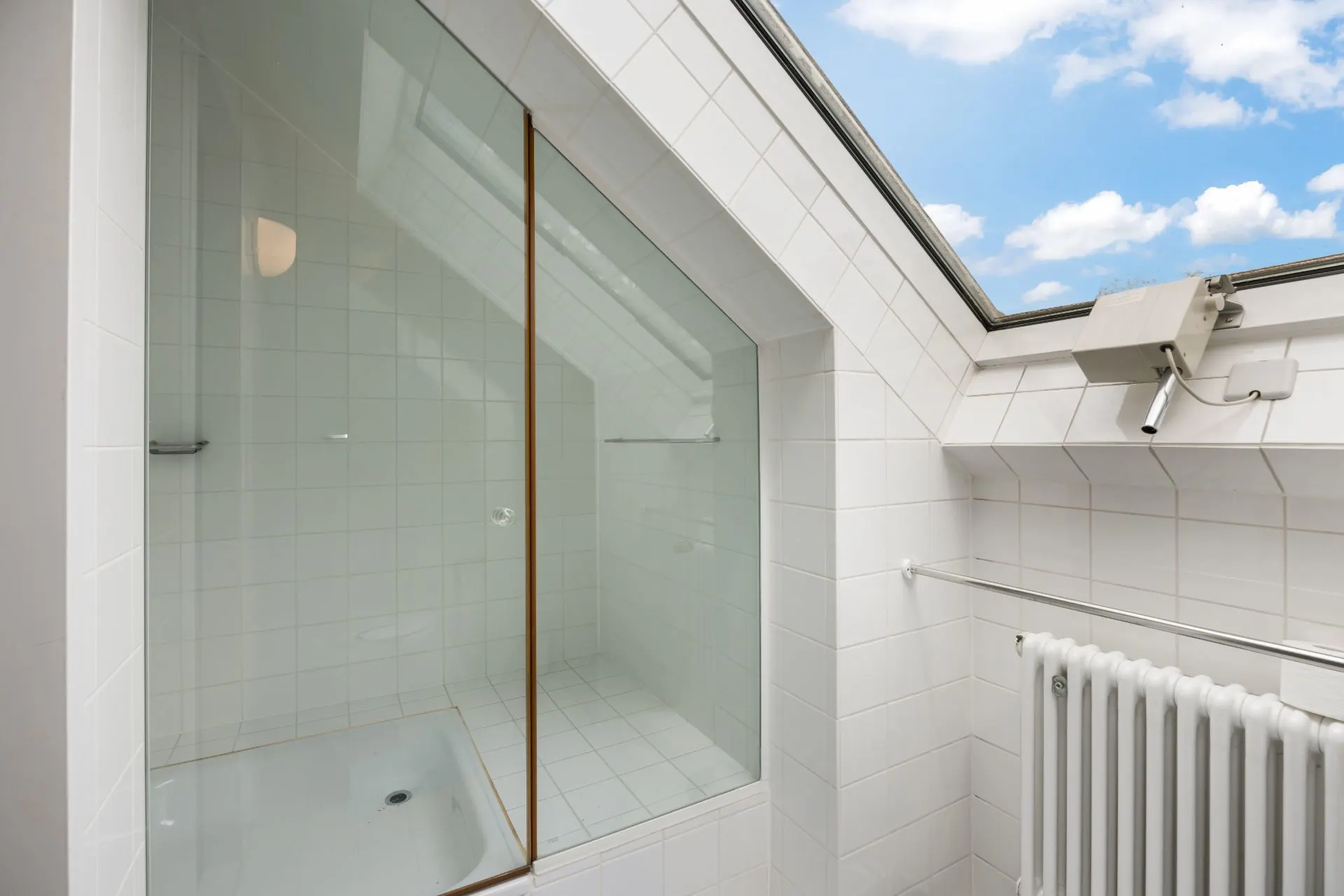 Modernes, weiß gefliestes Bad mit Dachfenster, Dusche und Heizkörper.