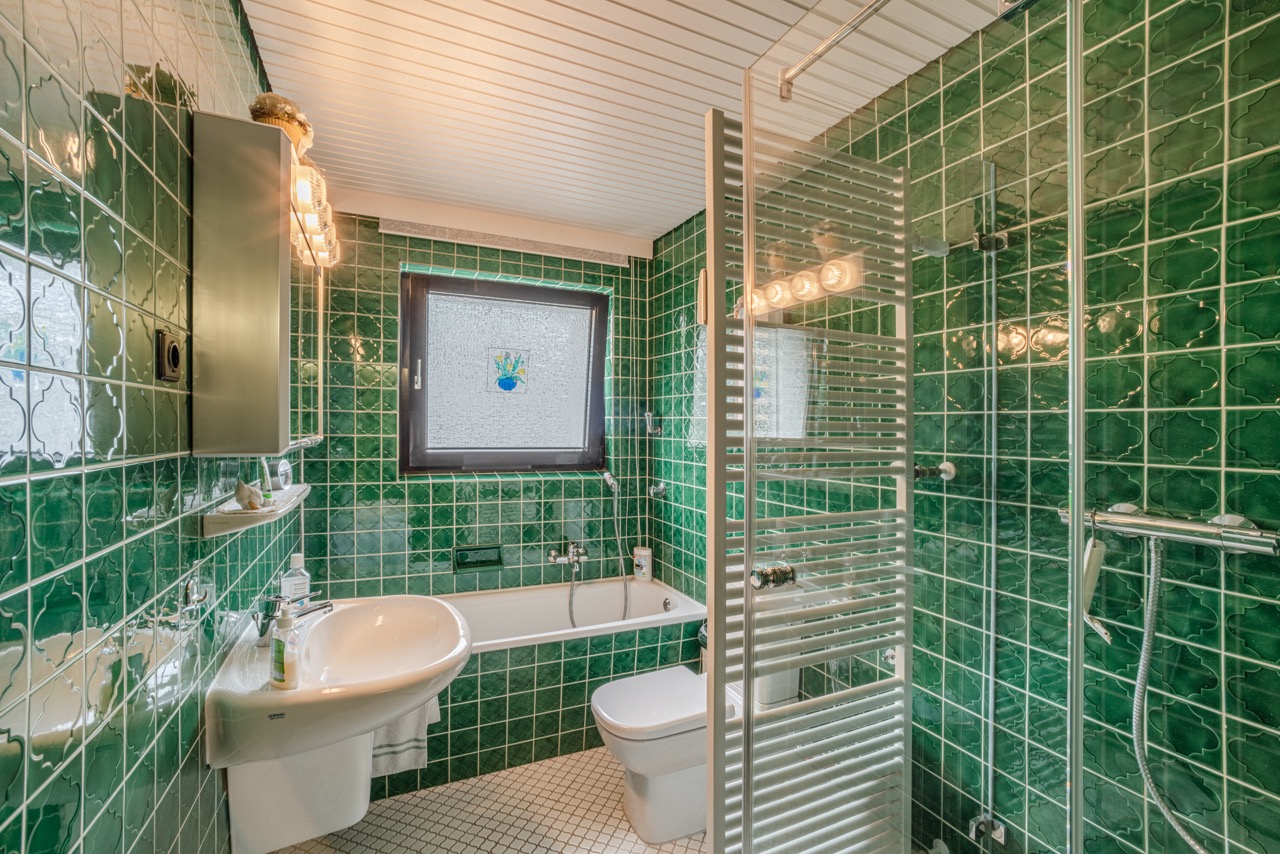 Grünes Badezimmer mit Badewanne, Dusche, Waschbecken, WC und Fenster.