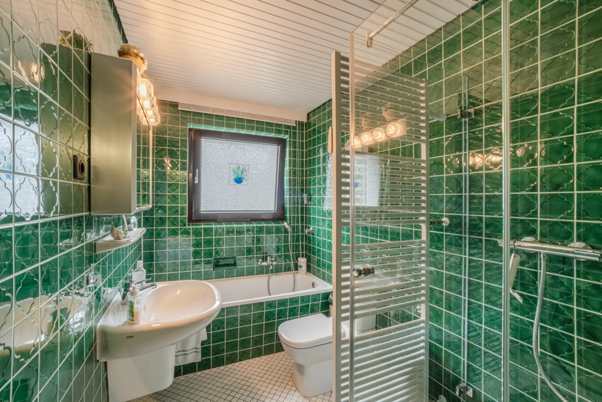 Grünes Badezimmer mit Badewanne, Dusche, Waschbecken, WC und Fenster.
