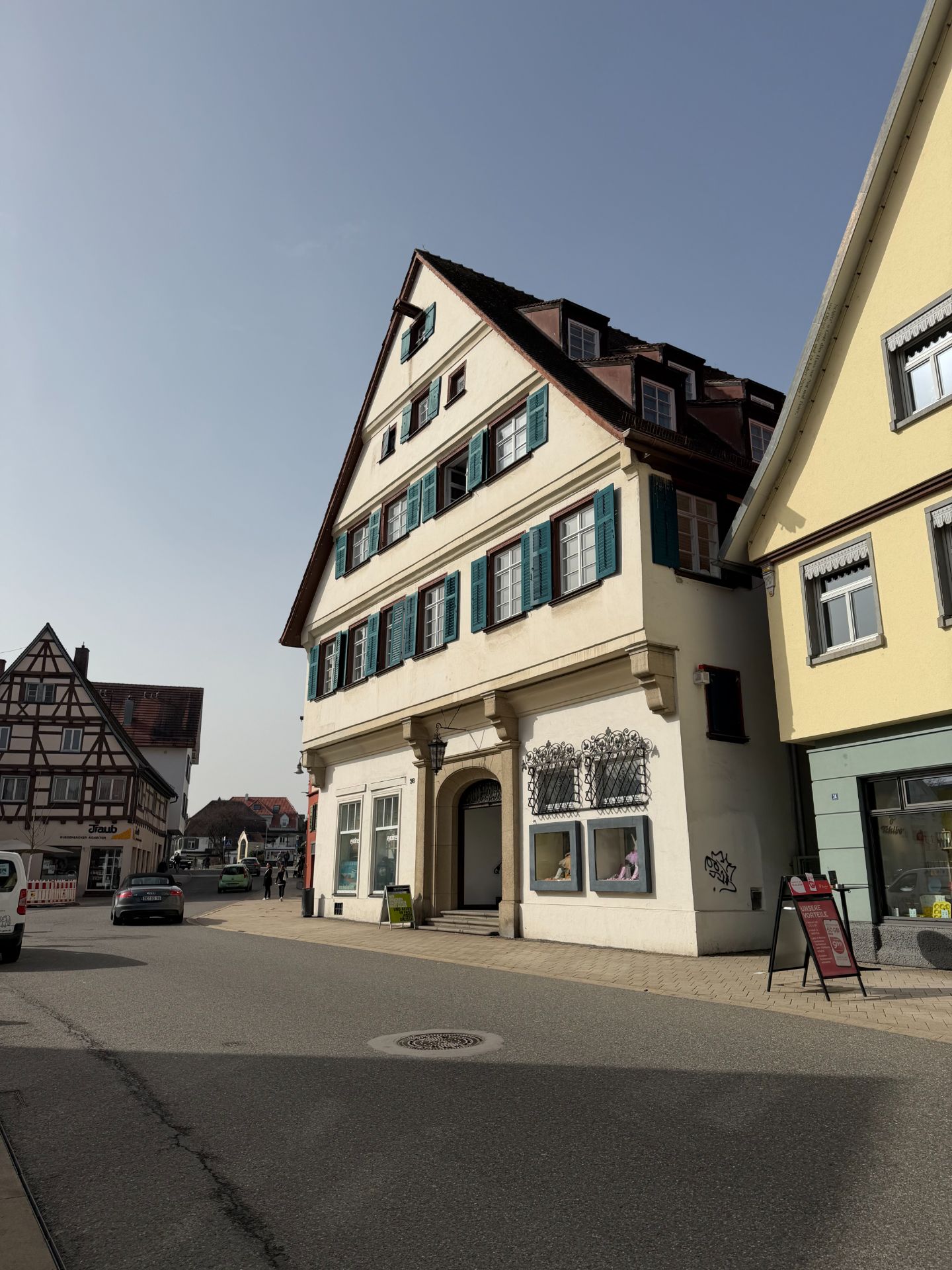 Großes historisches Wohnhaus mit grünen Fensterläden an einer ruhigen Straße bei Sonnenschein.