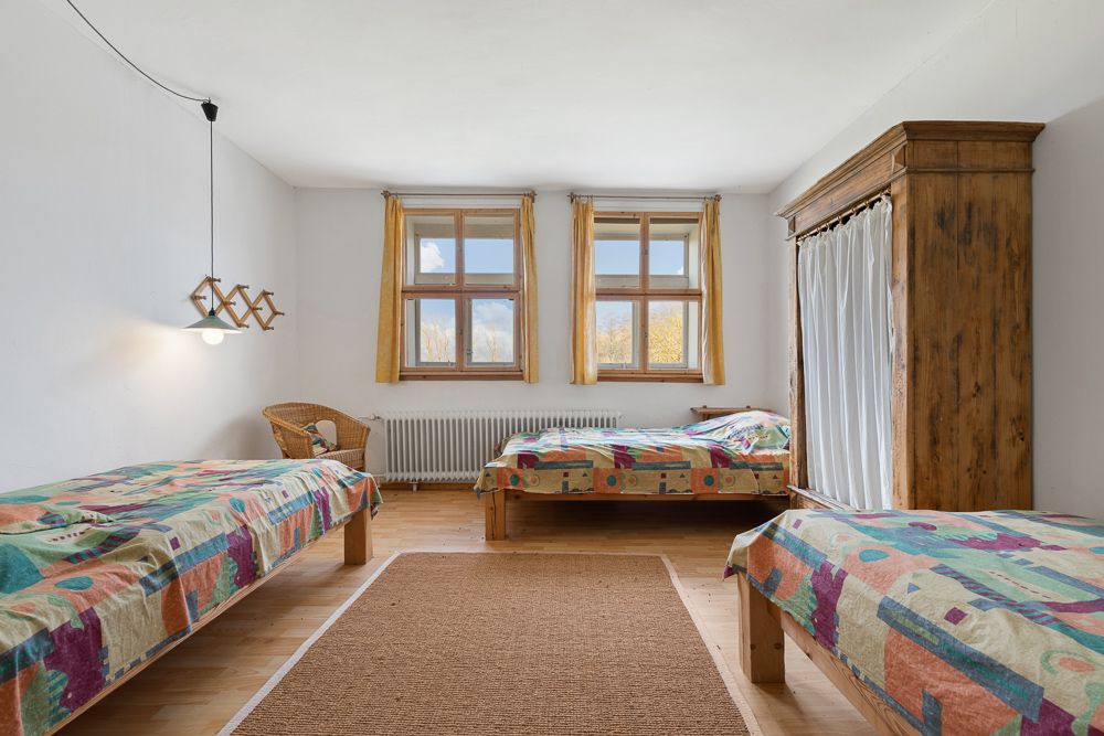 Helles Schlafzimmer mit drei Einzelbetten, Holzboden, großem Schrank und zwei Fenstern.