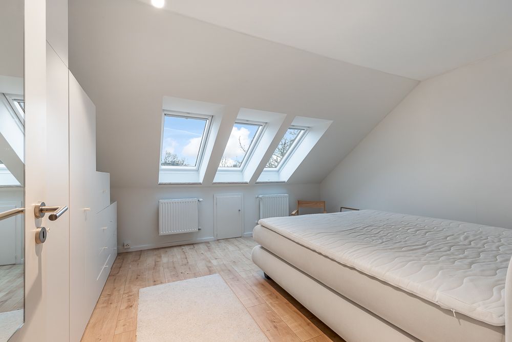 Helles Schlafzimmer mit Dachfenstern, Doppelbett, Kleiderschrank und Holzfußboden.