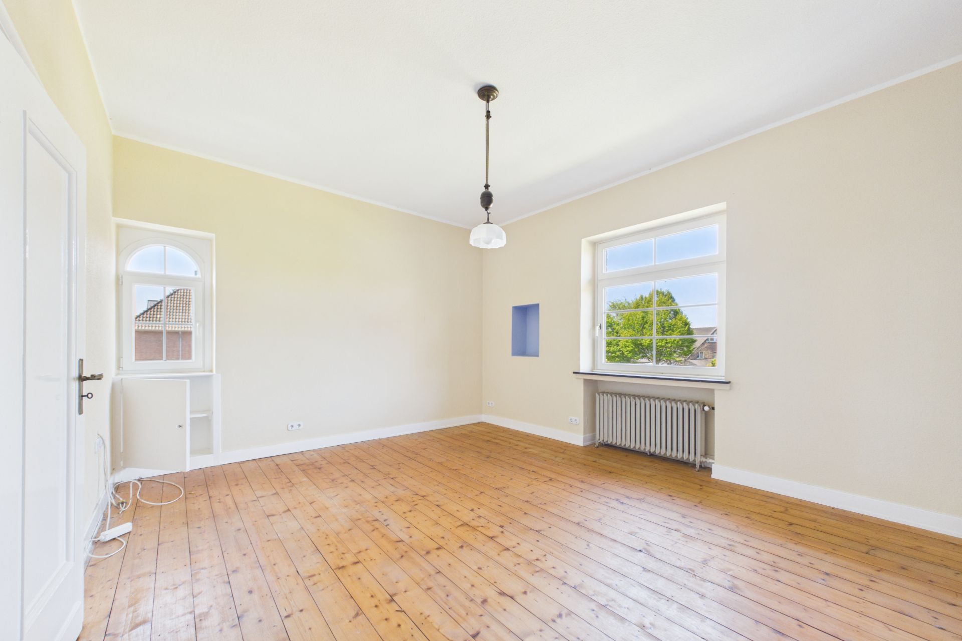 Helles, leeres Zimmer mit Holzboden, weißem Wandanstrich und zwei Fenstern.