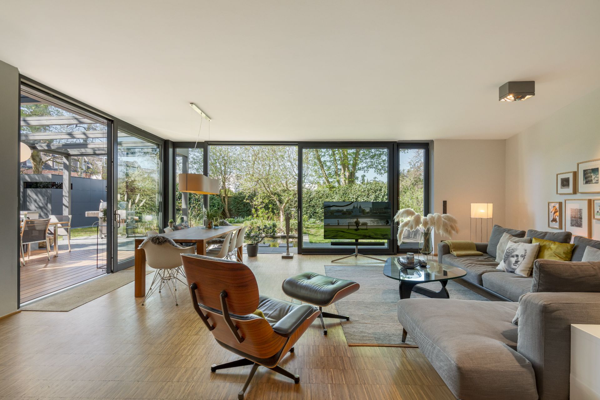 Modernes Wohnzimmer mit großen Fenstern, Sofa, Sessel, Esstisch und Blick in den Garten.