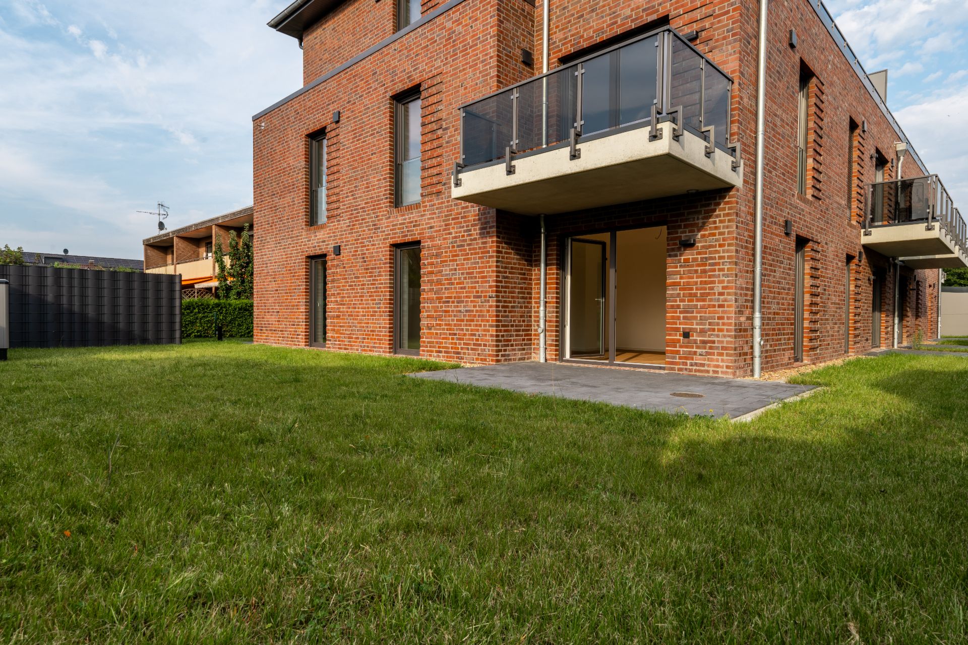 Backsteinwohnhaus mit Balkon, Terrasse und Rasenfläche im Vordergrund.