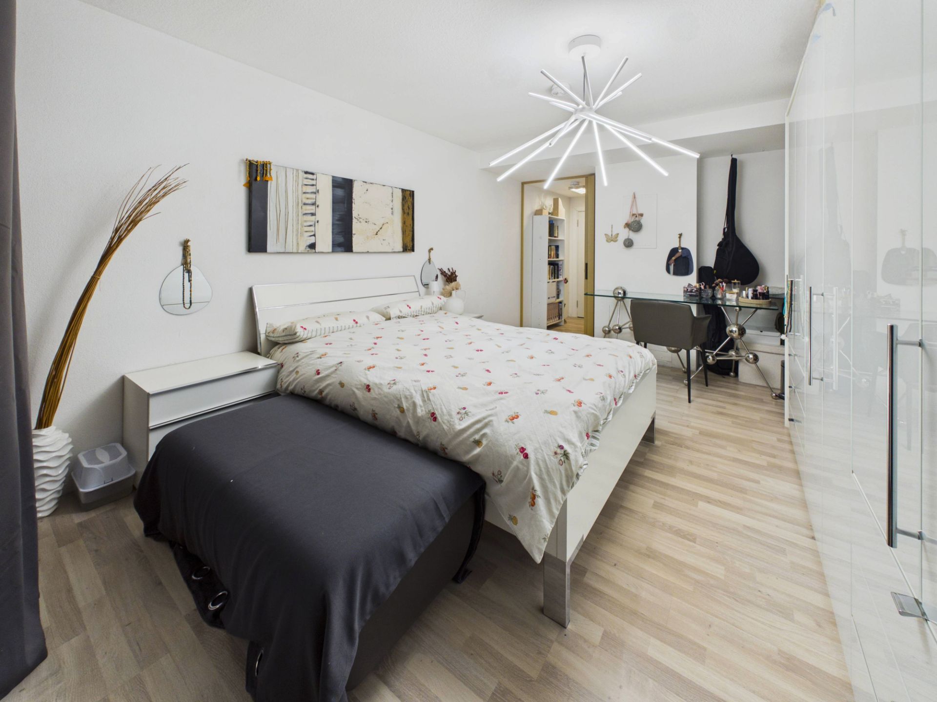 Helles Schlafzimmer mit Doppelbett, Schreibtisch, großem Schrank und modernem Kronleuchter.