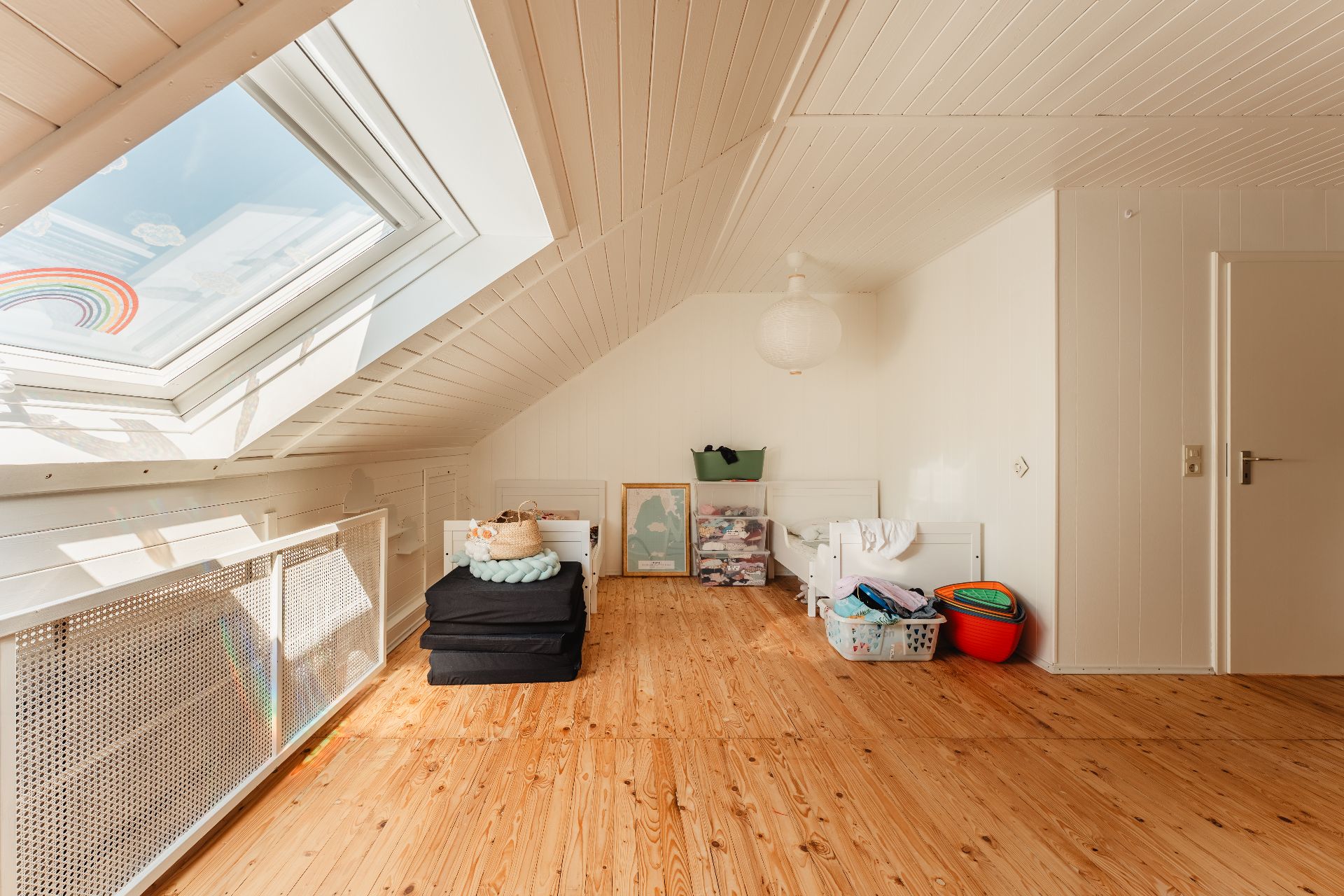 Dachzimmer mit Holzboden, zwei Betten und großem Dachfenster, viel Tageslicht.