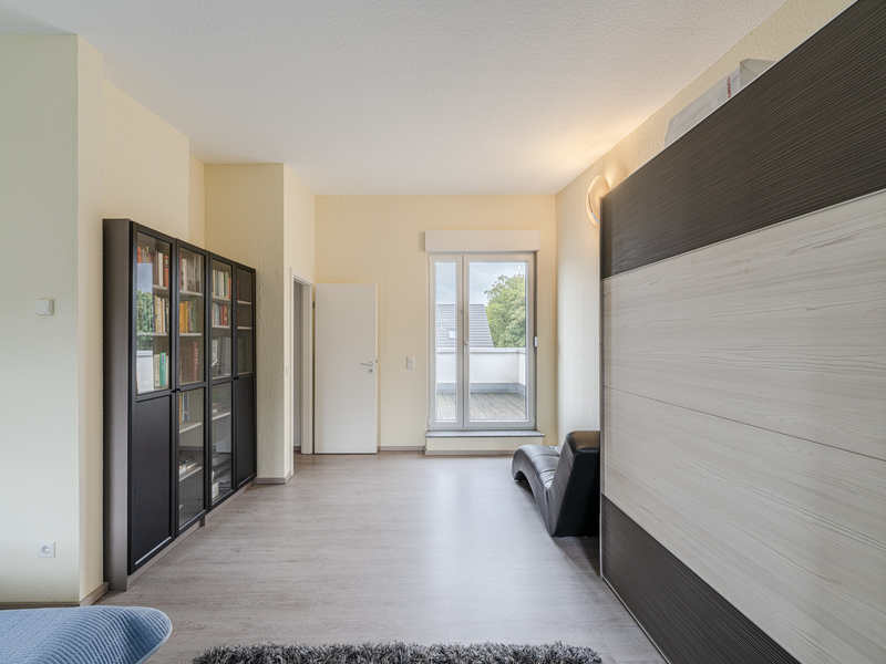 Helles Wohnzimmer mit Bücherregal, Tür, Balkonfenster und modernem Schrank.