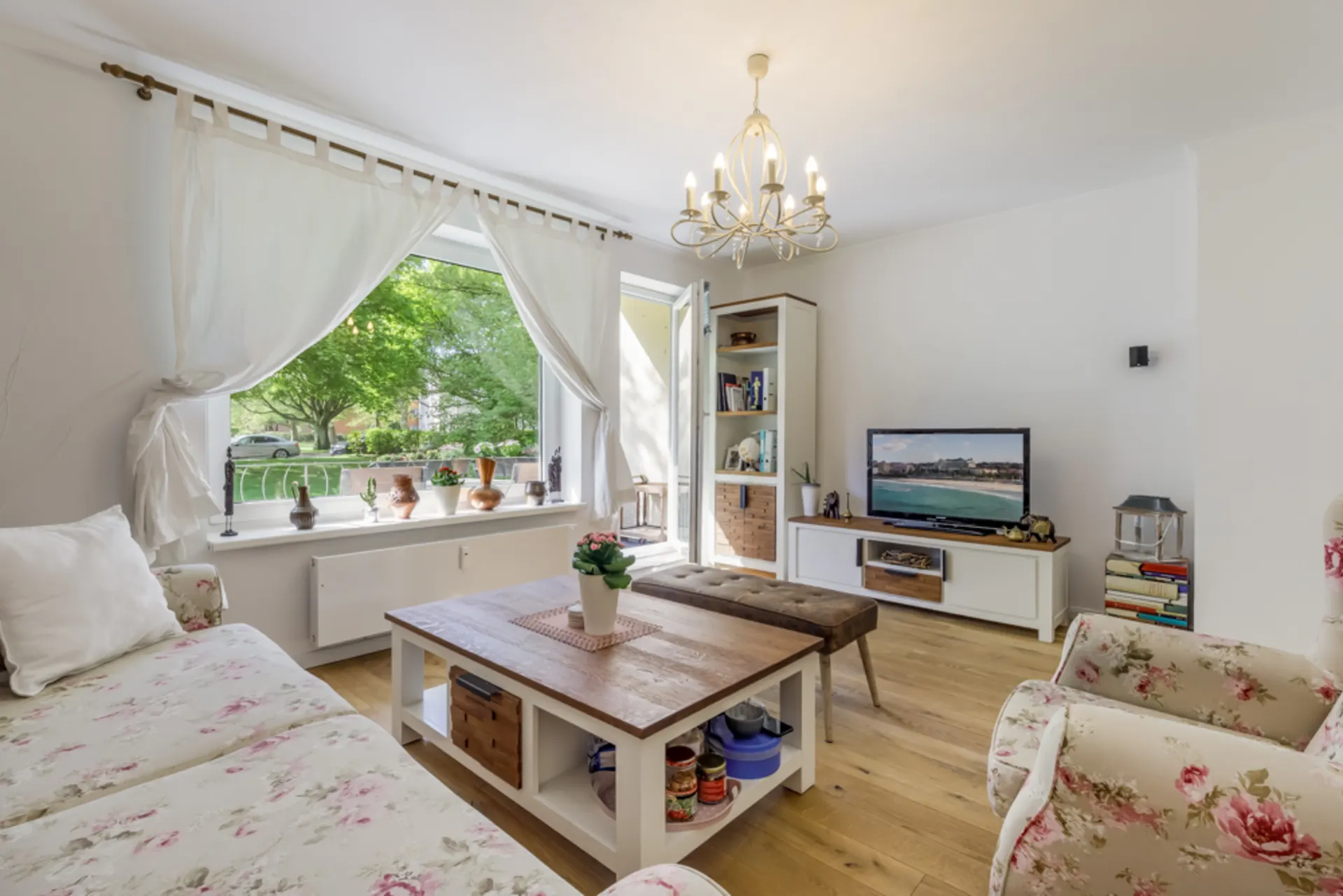 Helles Wohnzimmer mit Blumenmustermöbeln, großem Fenster, Fernseher und Holztisch.