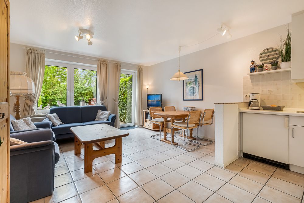Helles Wohnzimmer mit Sofa, Couchtisch, Essbereich, Küchenzeile und Blick in den Garten.