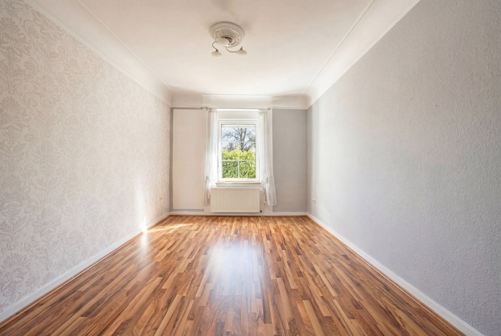Leerer Raum mit hellem Holzboden, weißem Fenster und grauen Wänden.