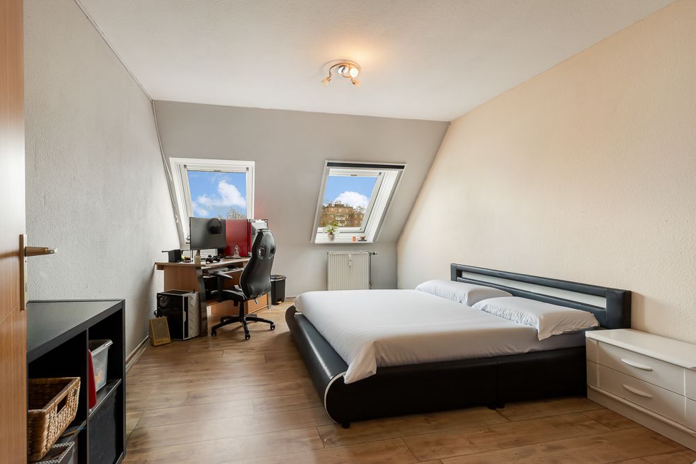 Helles Schlafzimmer mit Doppelbett und Schreibtisch unter zwei Dachfenstern.