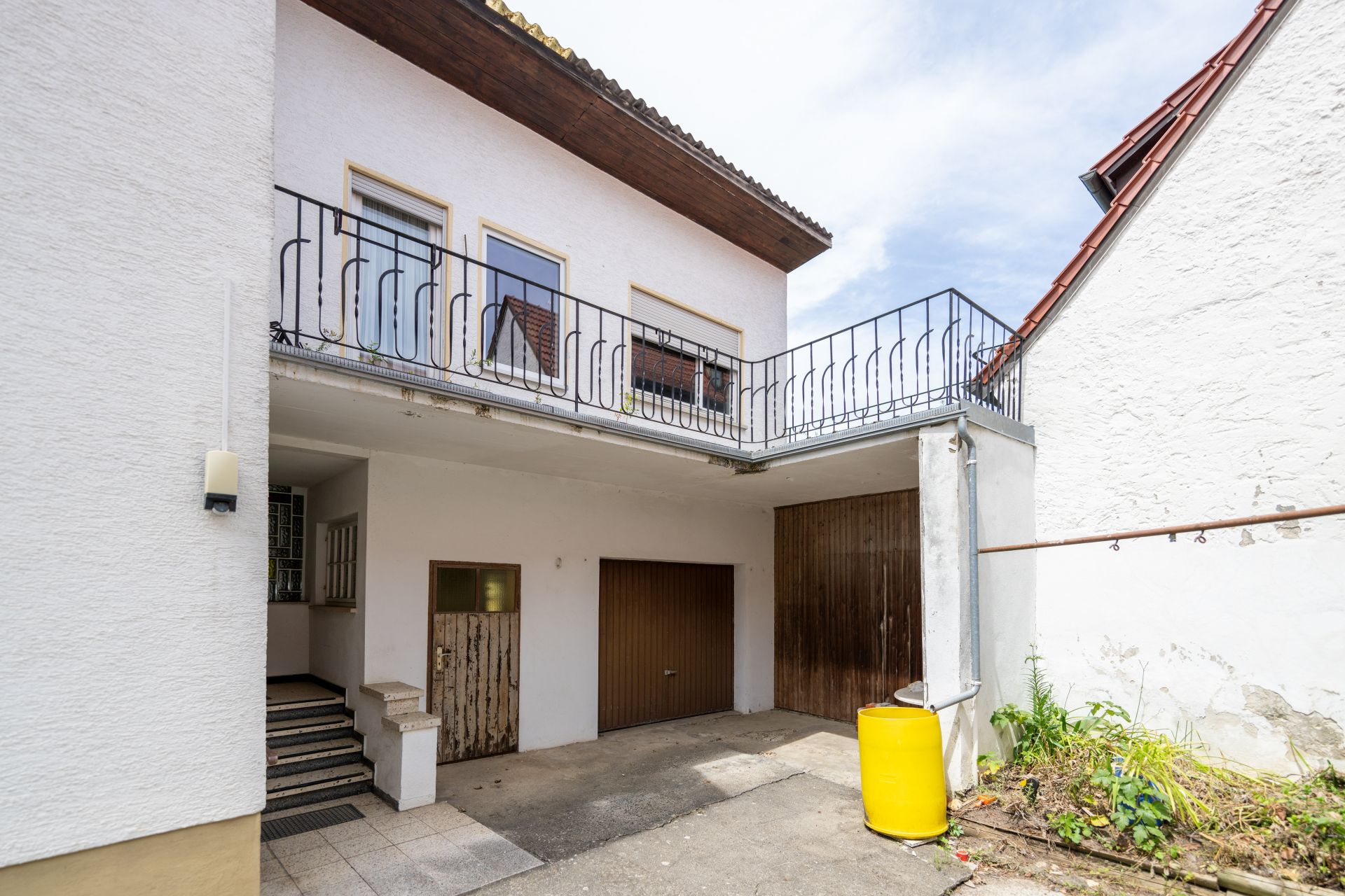 Innenhof eines Wohnhauses mit Balkon, Garage, Geländer und gelber Regentonne.