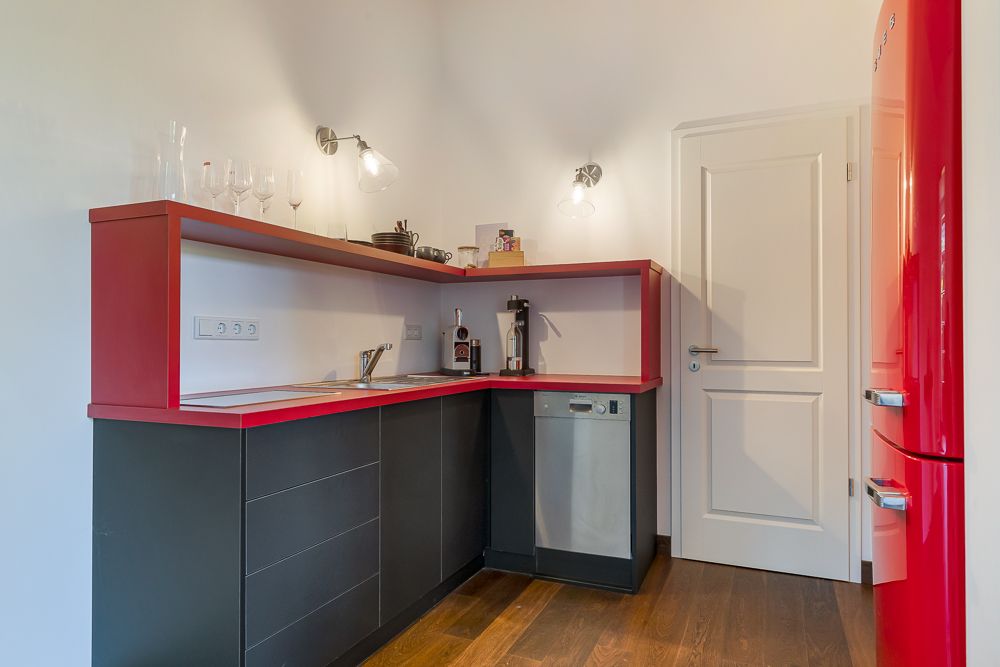 Moderne Küche mit roten Akzenten, Spüle, Geschirrspüler, rotem Kühlschrank und Gläsern auf der Theke.