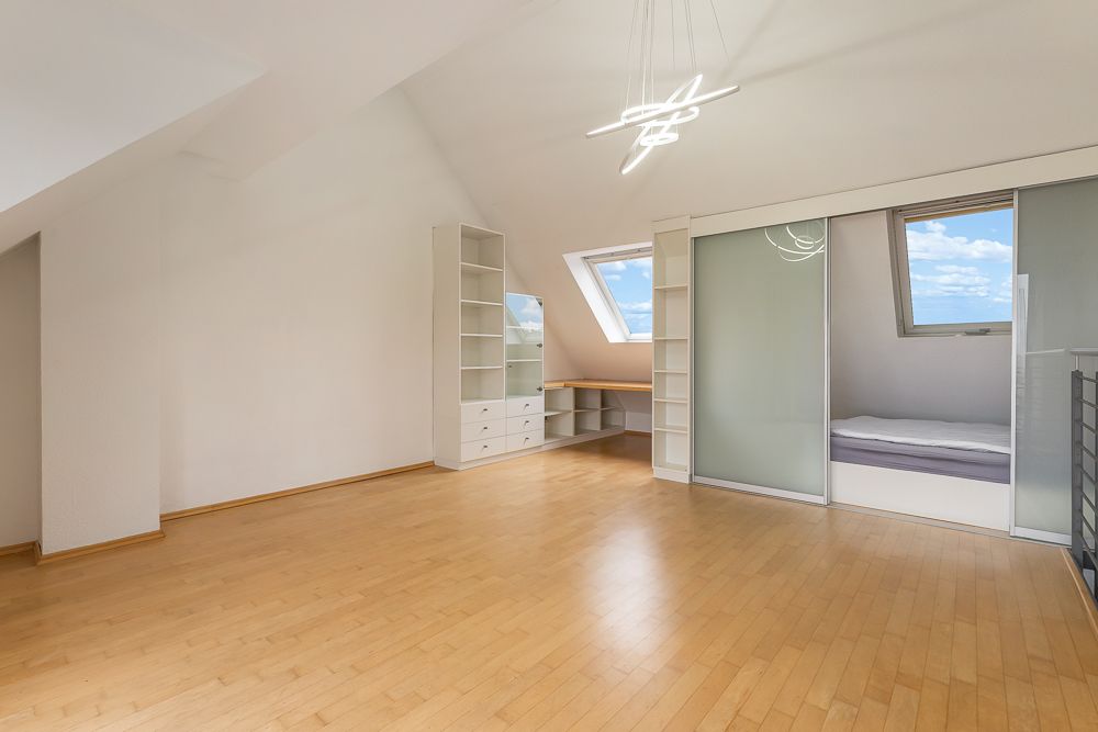Helles Zimmer mit Holzfußboden, Einbauregalen, Schreibtisch, Bett und großen Fenstern.