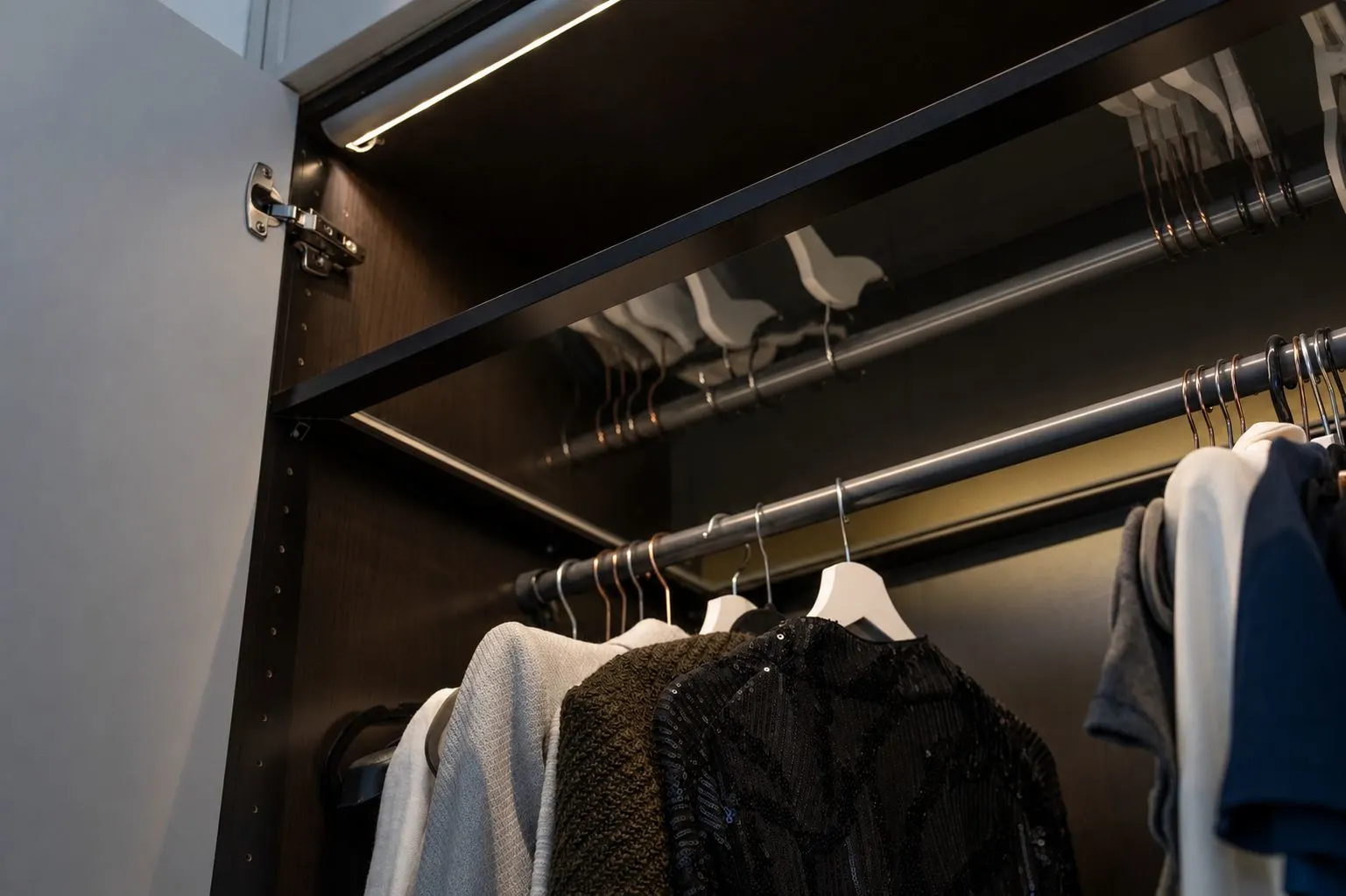 Offener Kleiderschrank mit Kleiderbügeln und mehreren Kleidungsstücken auf Stange.