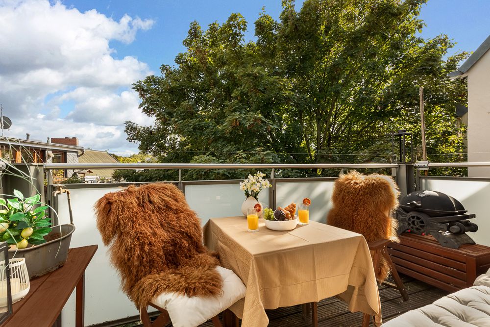 Balkon mit Tisch, zwei Stühlen mit Fellauflagen und Blick auf grüne Bäume.