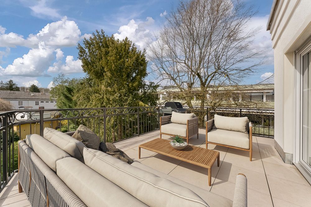 Sonnige Terrasse mit Sitzmöbeln, Tisch und Ausblick auf Bäume und Nachbarhäuser.
