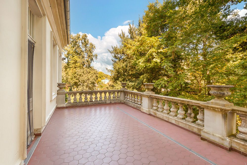 Große Terrasse mit roten Fliesen und steinernem Geländer, umgeben von Bäumen.