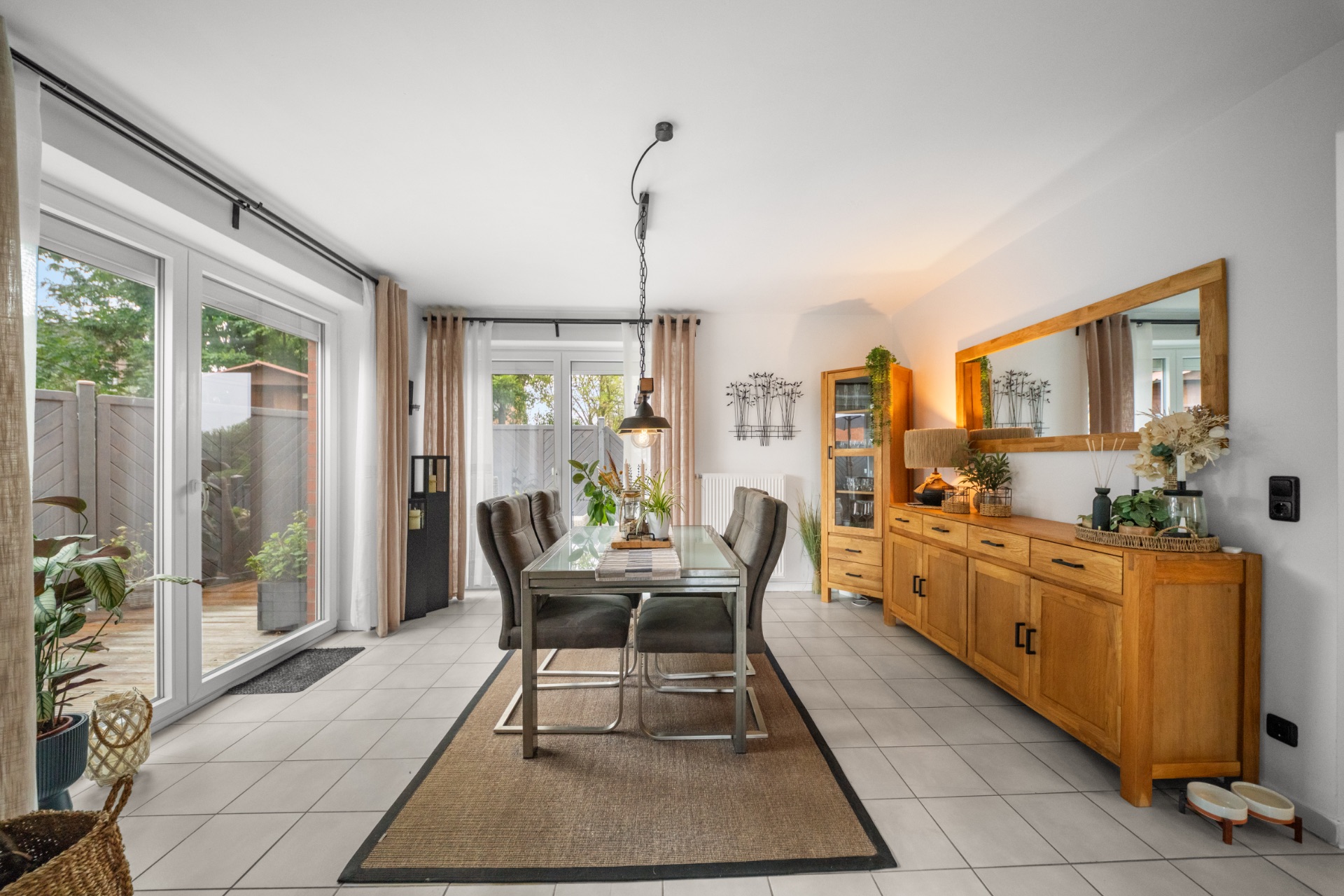 Esszimmer mit Glastisch, sechs Stühlen, großem Spiegel und Zugang zur Terrasse.