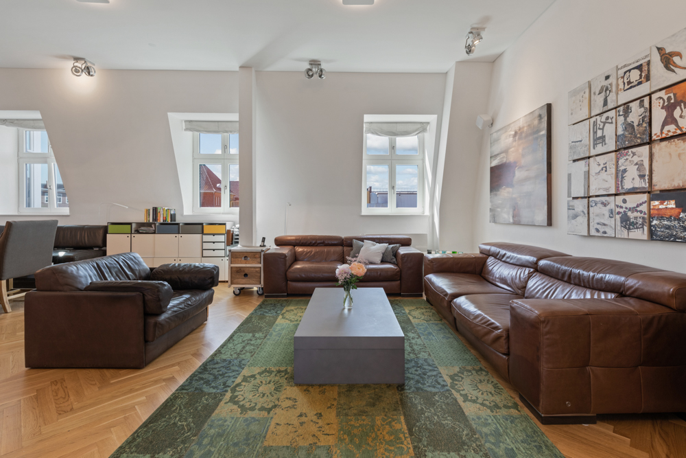 Modernes Wohnzimmer mit braunen Ledersofas, großem grünem Teppich und Bildern an der Wand.