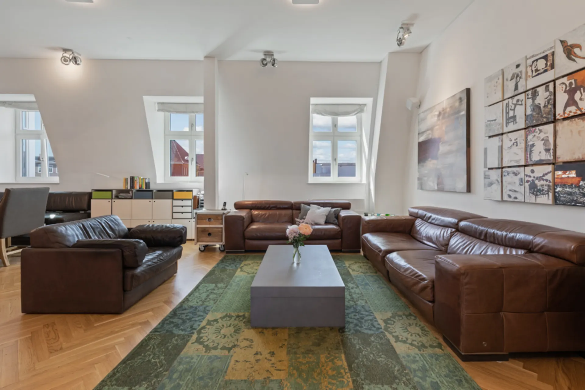 Modernes Wohnzimmer mit braunen Ledersofas, großem grünem Teppich und Bildern an der Wand.
