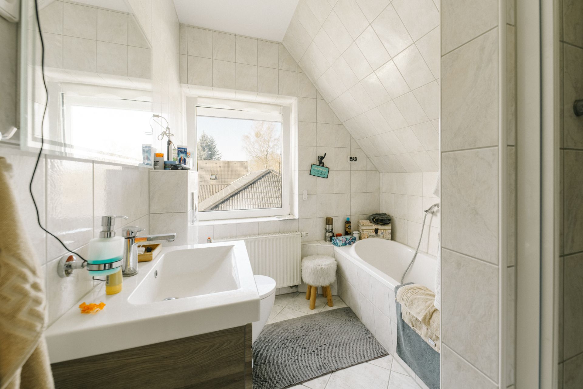 Helles Badezimmer mit Badewanne, Waschbecken, zwei Fenstern und Dachschräge.