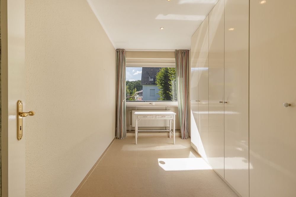 Helles Zimmer mit großem Fenster, Schrankwand und kleinem Tisch unter dem Fenster.