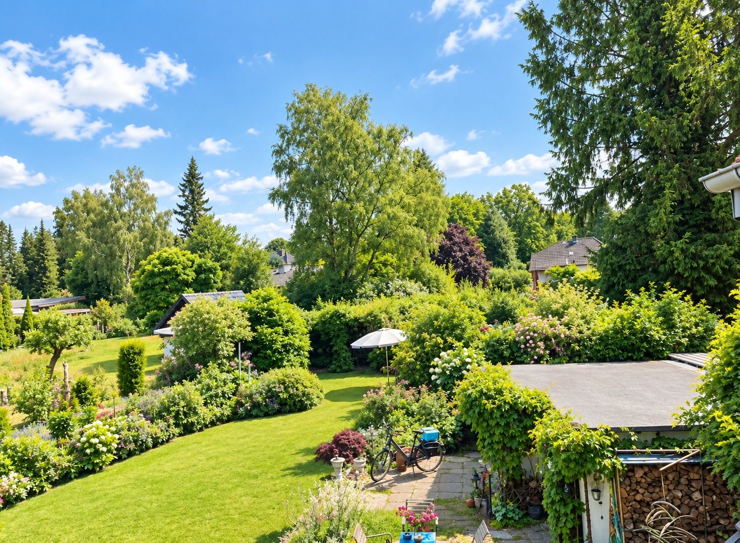 Großer Garten mit Rasen, Blumen, Bäumen, Schuppen, Fahrrad und Sonnenschirm bei sonnigem Wetter.