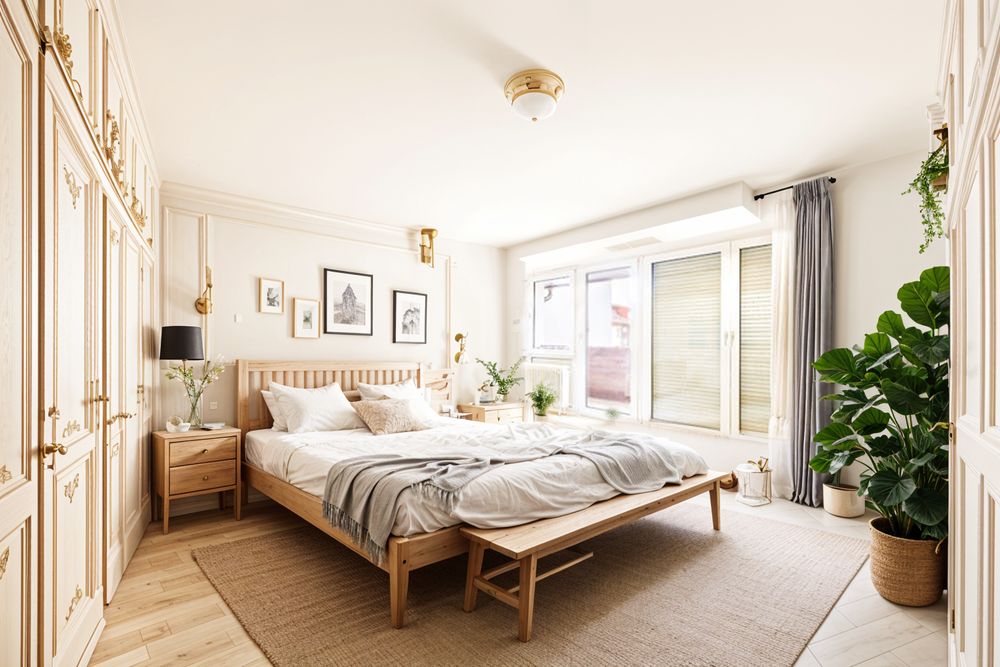 Helles Schlafzimmer mit Doppelbett, großen Fenstern, Pflanzen und Holzmöbeln.