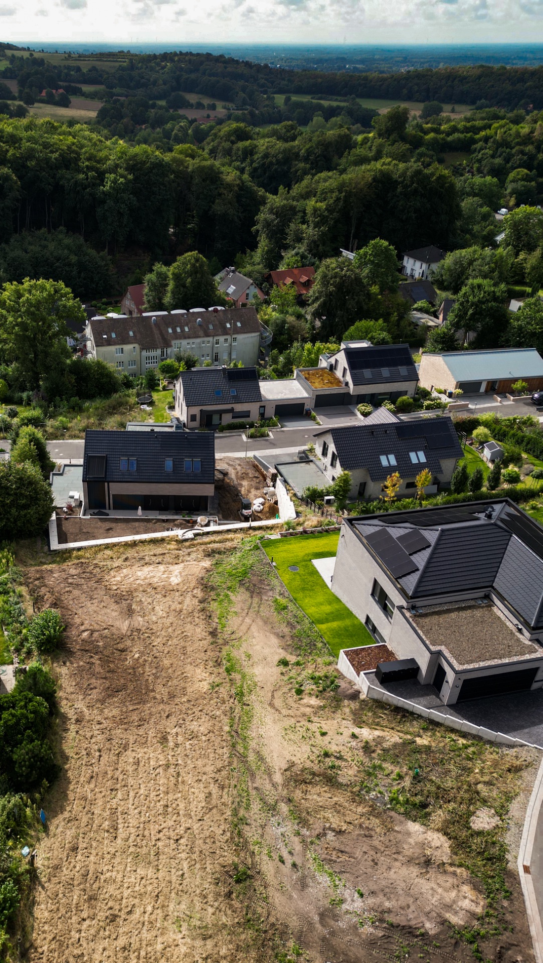 Luftaufnahme von modernen Einfamilienhäusern mit Gärten und umliegendem Wald.