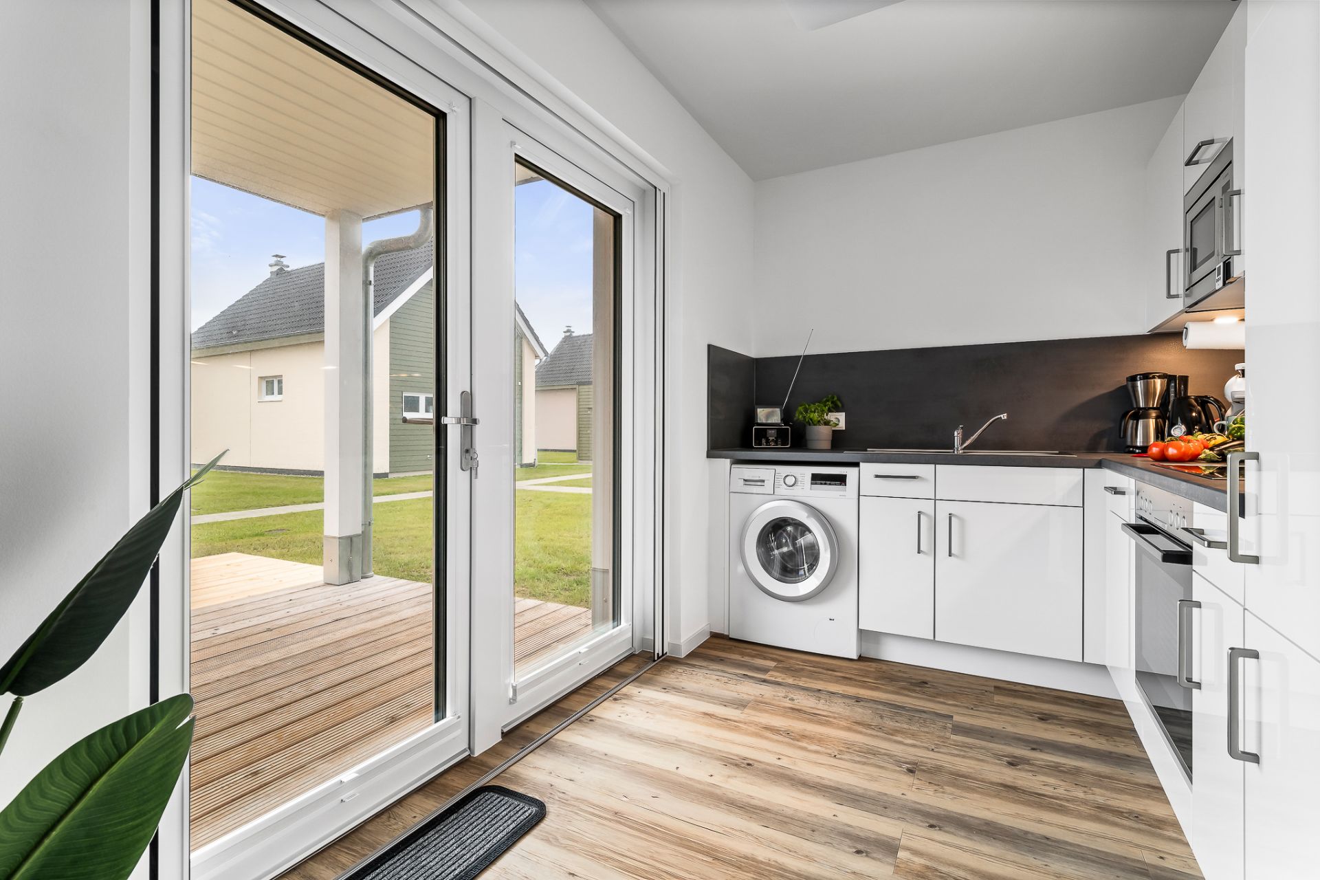 Helle Küche mit Waschmaschine, weißen Schränken und Zugang zur Terrasse durch große Glastüren.