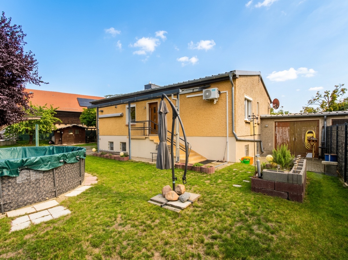 Garten mit Pool, Sonnenschirm und gelbem Haus mit Treppe und Garage im Hintergrund.