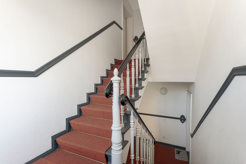 Rotes Treppenhaus mit weißem Geländer und schwarzen Handläufen in einem Wohnhaus.