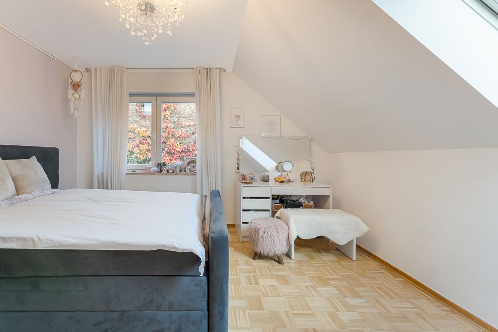 Helles Schlafzimmer mit großem Bett, Schminktisch, Fenster und schräger Decke.