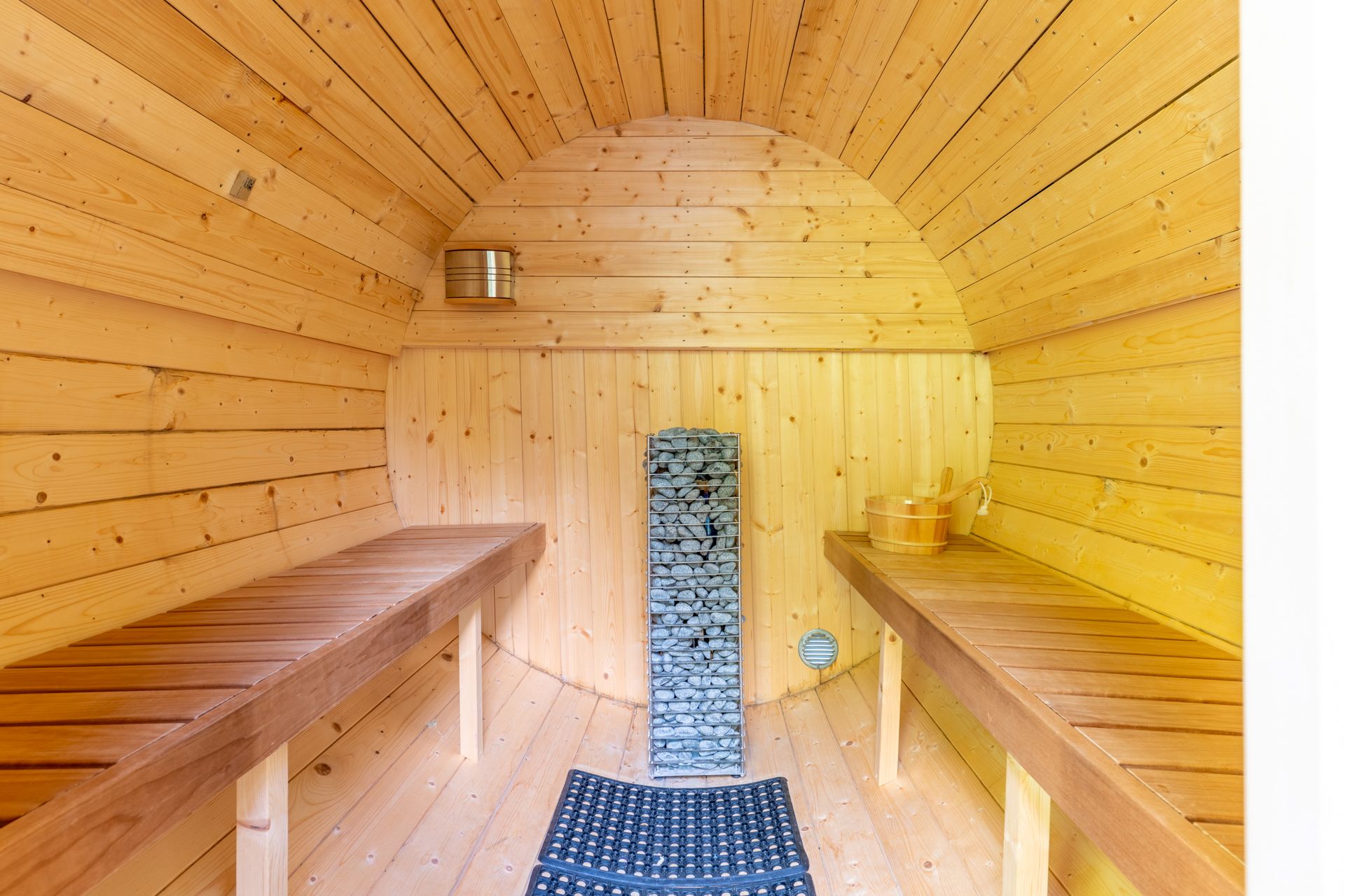 Innenraum einer Holzsauna mit zwei Bänken, einem Saunaofen und Eimer.