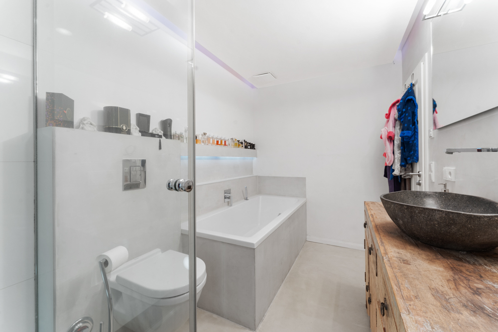 Modernes Badezimmer mit Badewanne, Wandtoilette, Waschbecken und Holzkommode.
