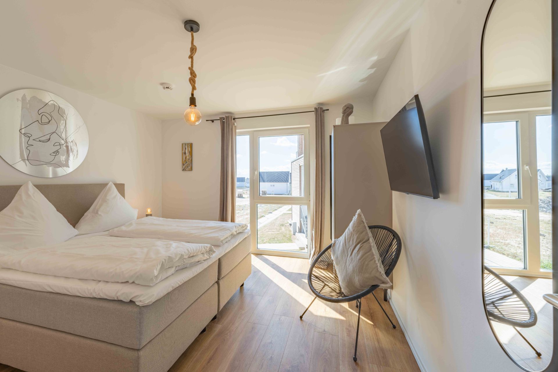 Helles Schlafzimmer mit Doppelbett, Stuhl, großem Fenster und Wandspiegel.