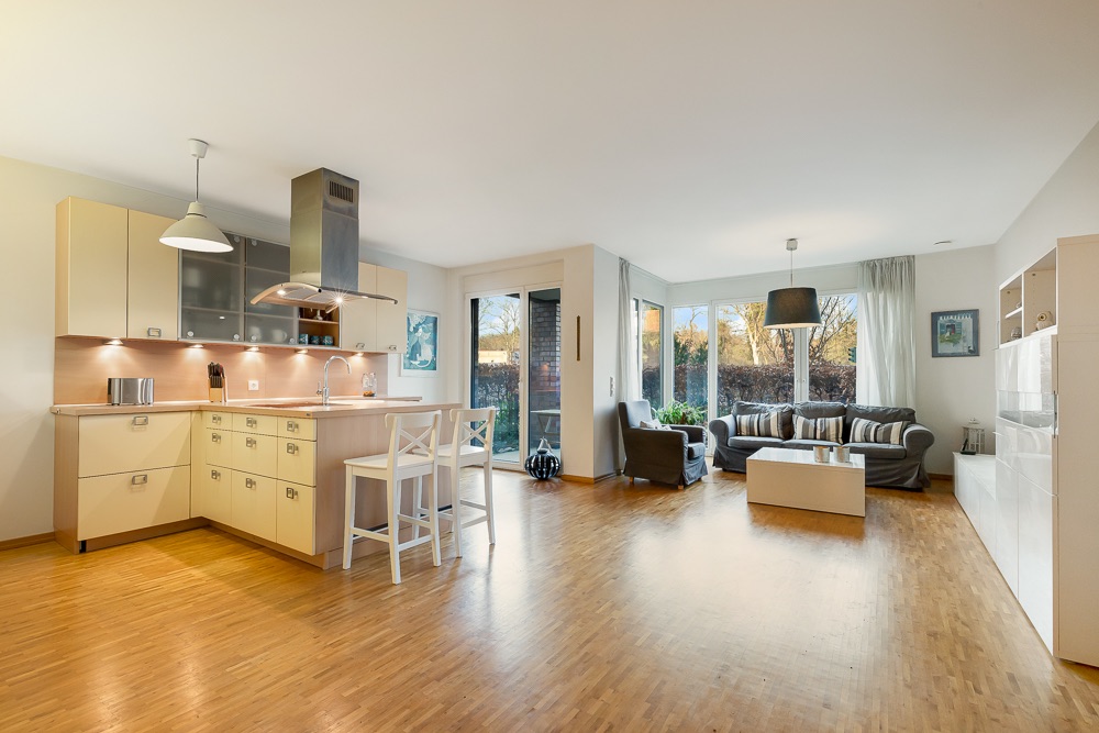 Helles Wohnzimmer mit offener Küche, Essbereich, Sofa und großen Fenstern mit Blick in den Garten.