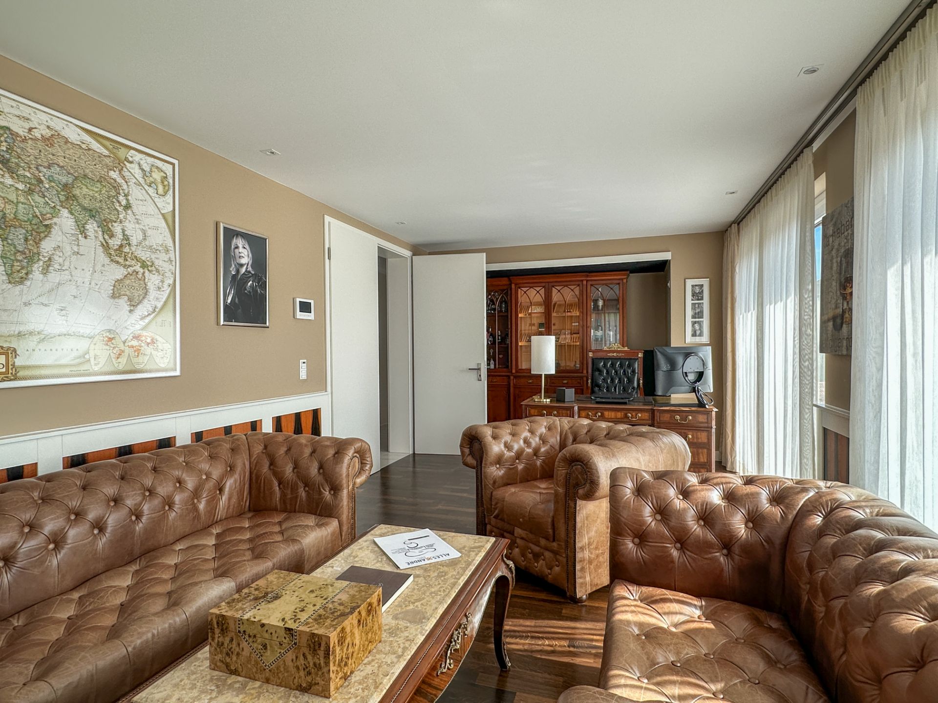 Wohnzimmer mit braunen Ledersofas, Holztisch und großem Fenster mit Vorhängen.