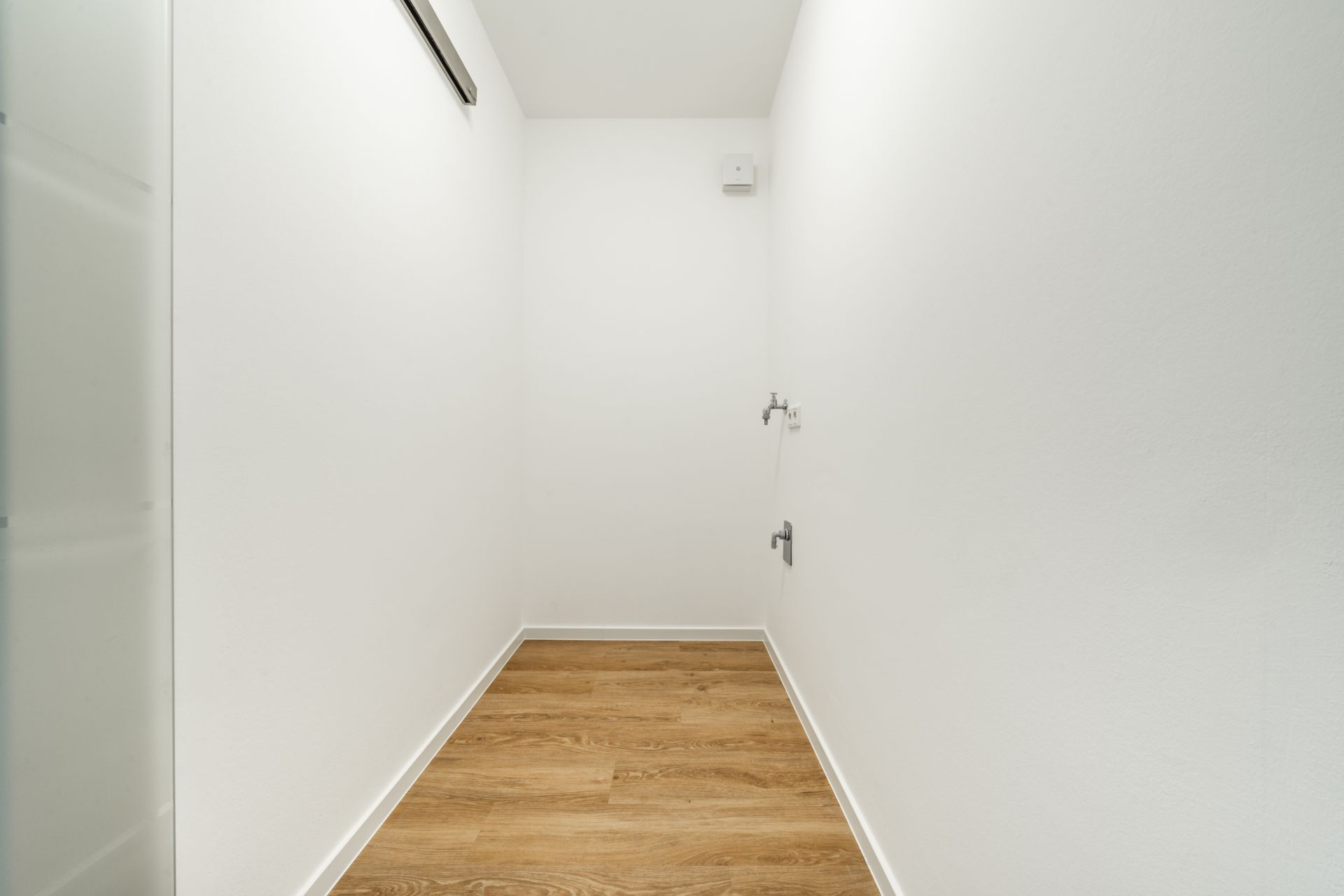 Schmaler Raum mit weiß gestrichenen Wänden und hellem Holzfußboden.